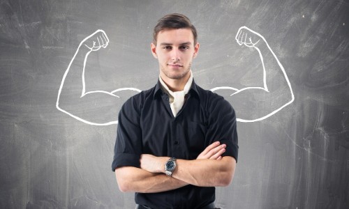 Man standing in front of chalkboard with strong muscles flexing drawn in behind him